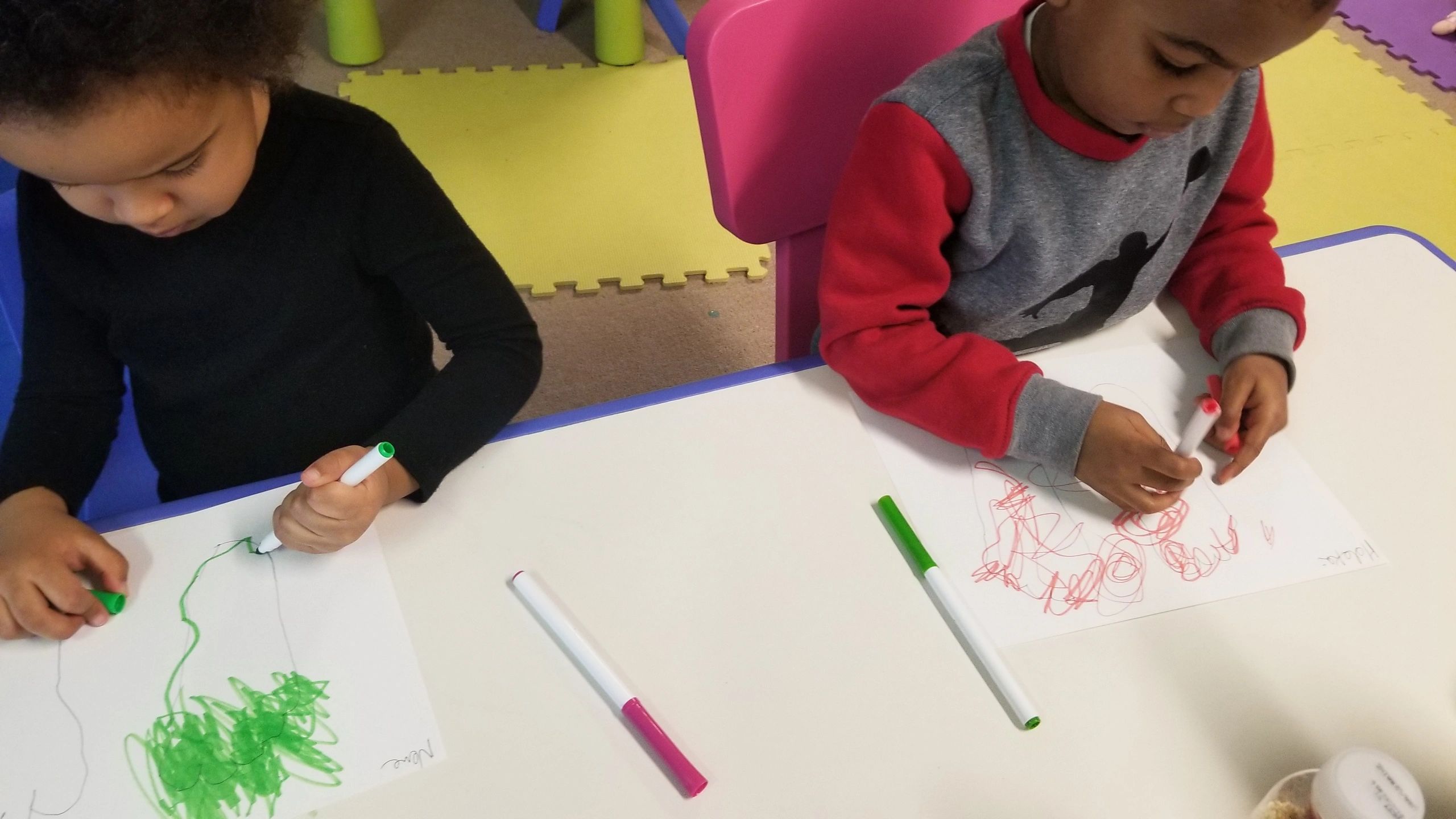 Two children drawing on paper at a table with markers